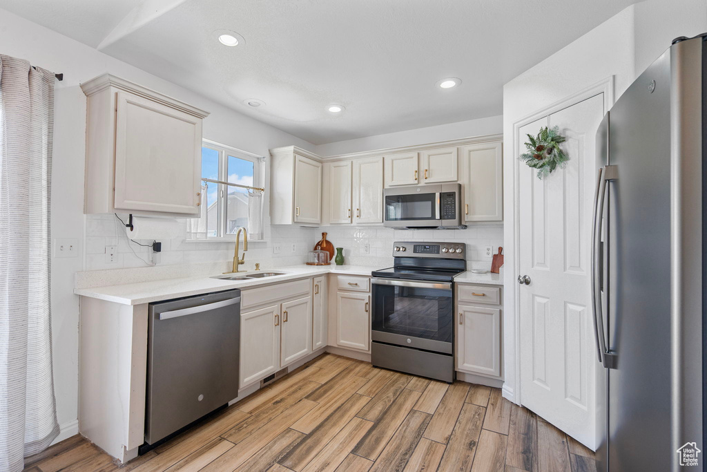 Kitchen with decorative backsplash, appliances with stainless steel finishes, a sink, and light wood-style flooring