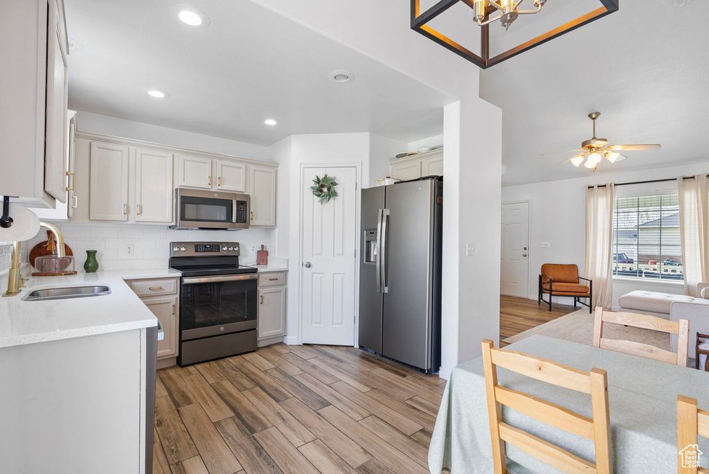 Kitchen with stainless steel appliances, light countertops, backsplash, a sink, and light wood-type flooring