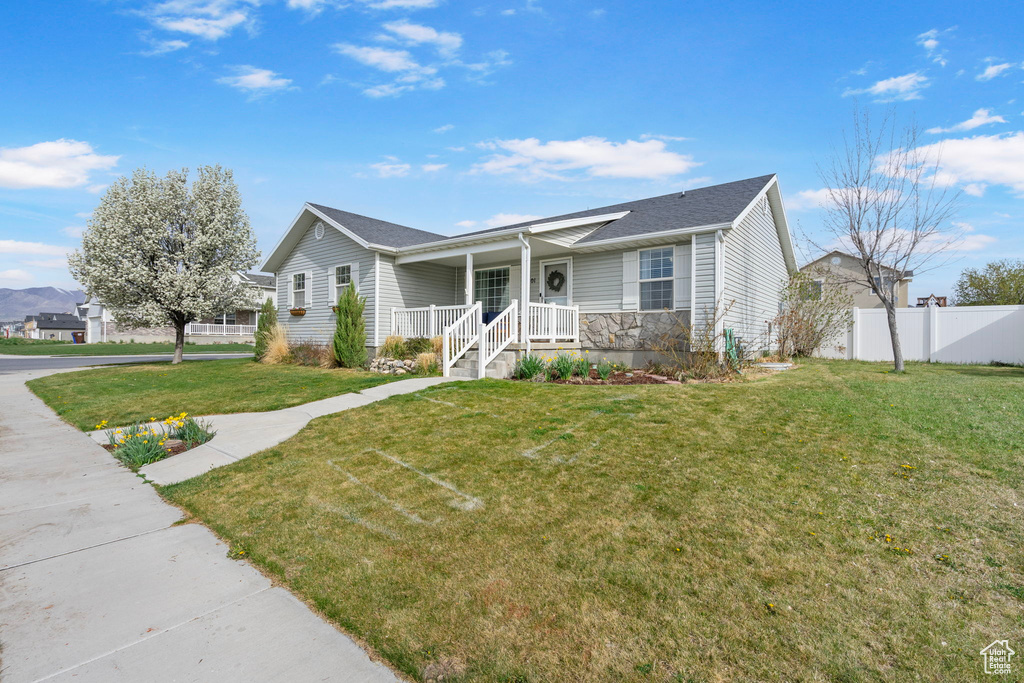 Ranch-style house with stone siding, fence, a front yard, and covered porch