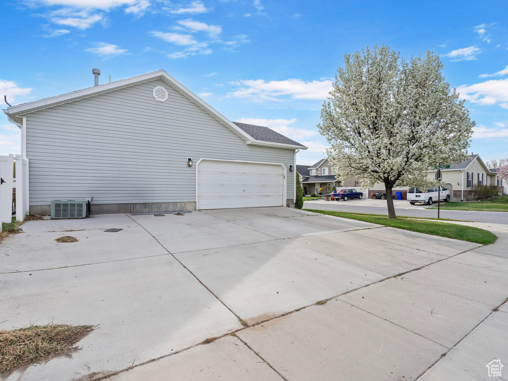 View of side of property with concrete driveway, central AC unit, fence, and a garage