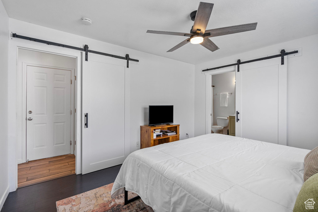 Bedroom with a barn door, a ceiling fan, dark wood-type flooring, and ensuite bathroom