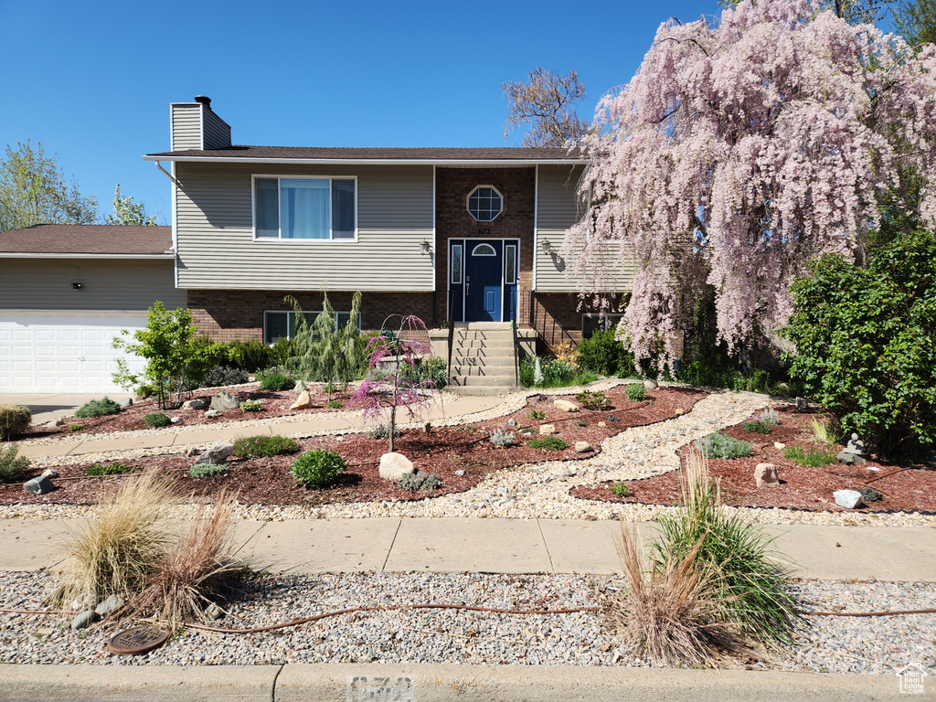 Bi-level home with a chimney, an attached garage, brick siding, and entry steps