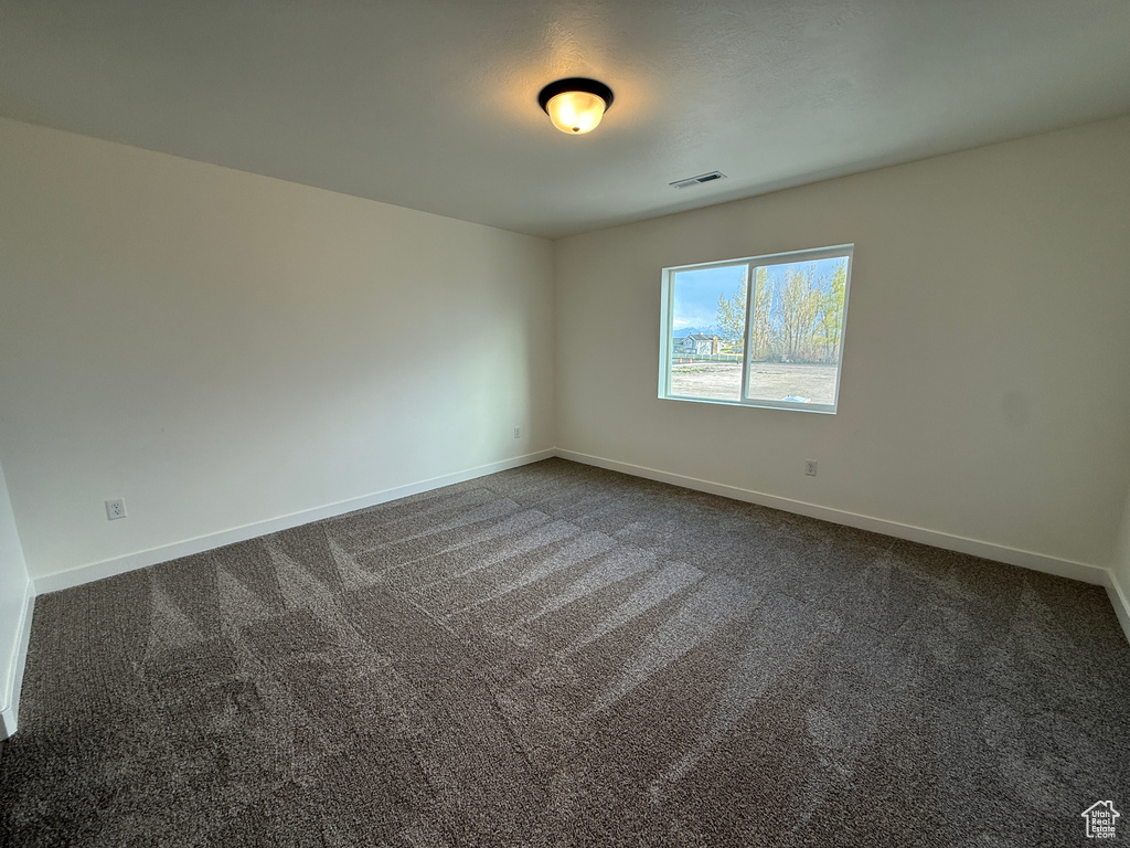 Spare room with baseboards, dark colored carpet, and visible vents