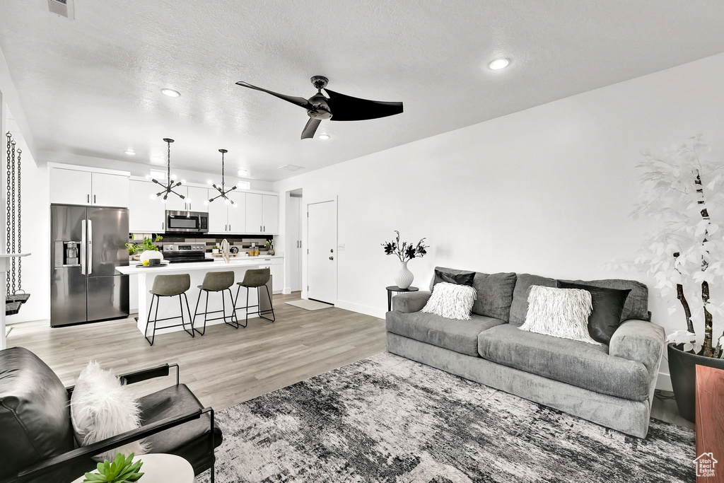 Living area with a chandelier, ceiling fan, recessed lighting, light wood finished floors, and baseboards