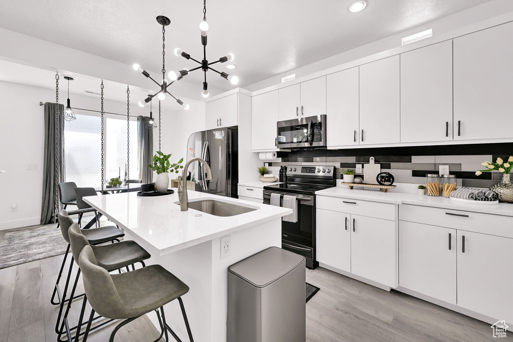 Kitchen with appliances with stainless steel finishes, a sink, light wood-style flooring, a breakfast bar, and recessed lighting