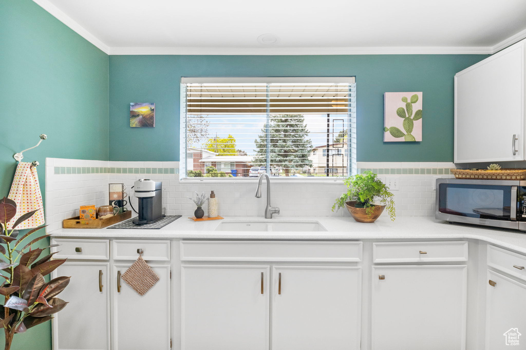 Kitchen with stainless steel microwave, backsplash, a sink, and white cabinets