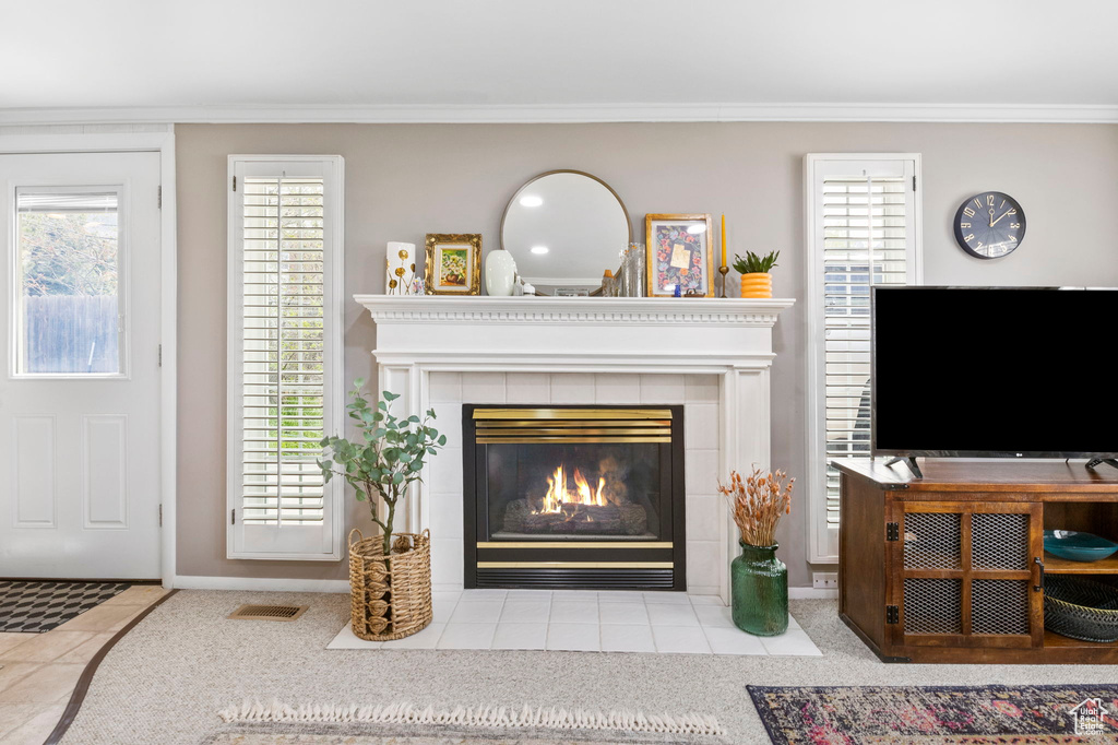 Carpeted living room with a tile fireplace, tile patterned floors, visible vents, ornamental molding, and a wealth of natural light
