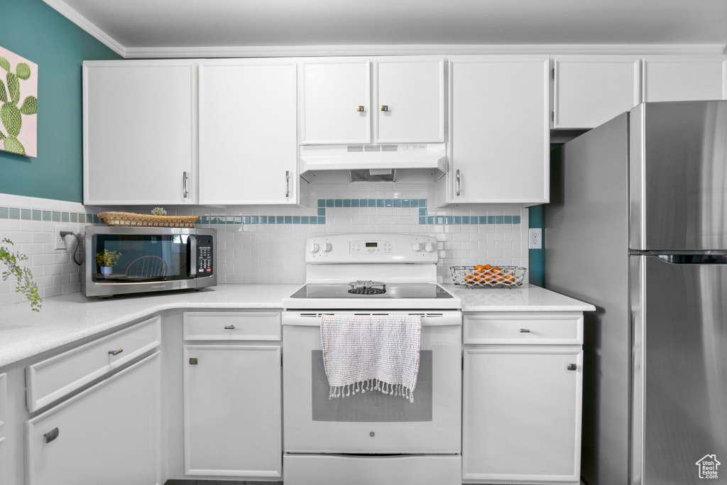 Kitchen with stainless steel appliances, light countertops, under cabinet range hood, and white cabinetry