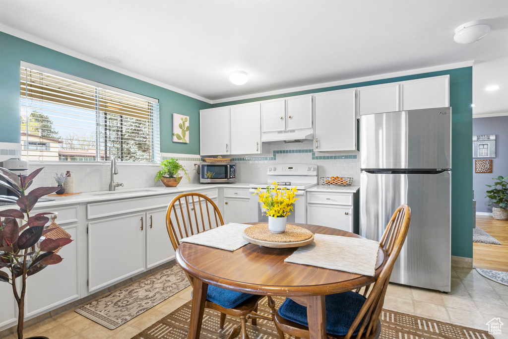 Kitchen with crown molding, a sink, appliances with stainless steel finishes, light countertops, and under cabinet range hood