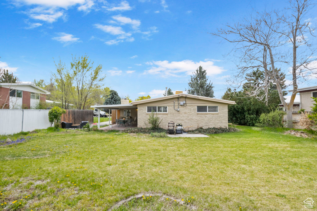 Rear view of property featuring a chimney, fence, a yard, and a patio