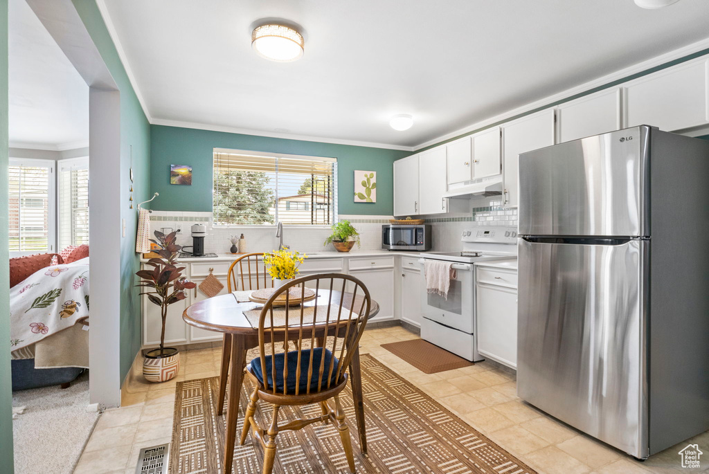 Kitchen featuring under cabinet range hood, stainless steel appliances, light countertops, ornamental molding, and white cabinetry