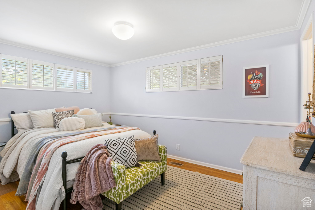 Bedroom with wood finished floors, visible vents, and ornamental molding