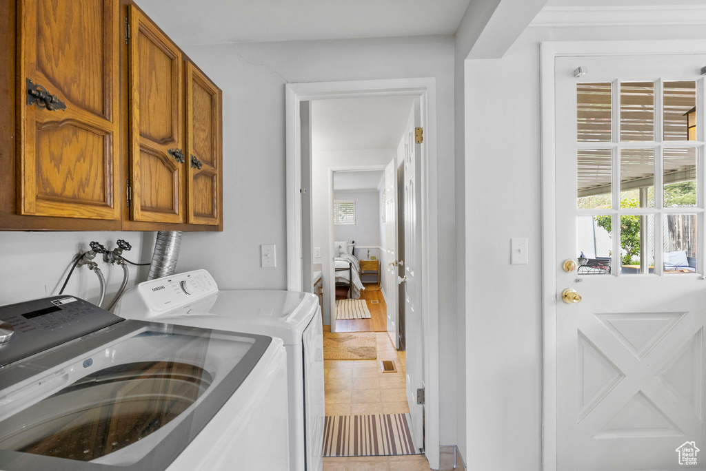 Laundry room with washing machine and clothes dryer, light tile patterned floors, and cabinet space