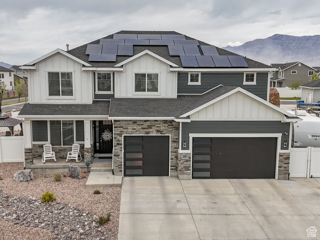 View of front of house featuring solar panels, a porch, stone siding, fence, and board and batten siding