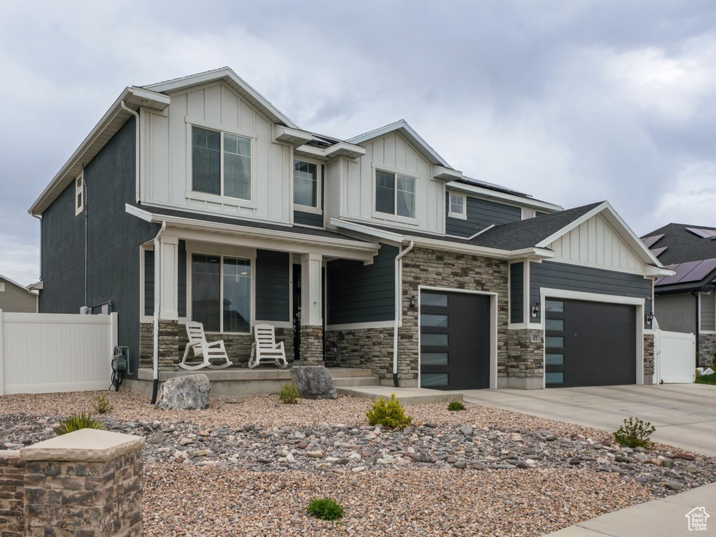 Craftsman-style house featuring concrete driveway, stone siding, board and batten siding, fence, and a porch