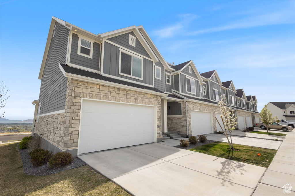 View of front of home with a garage, a residential view, stone siding, and concrete driveway