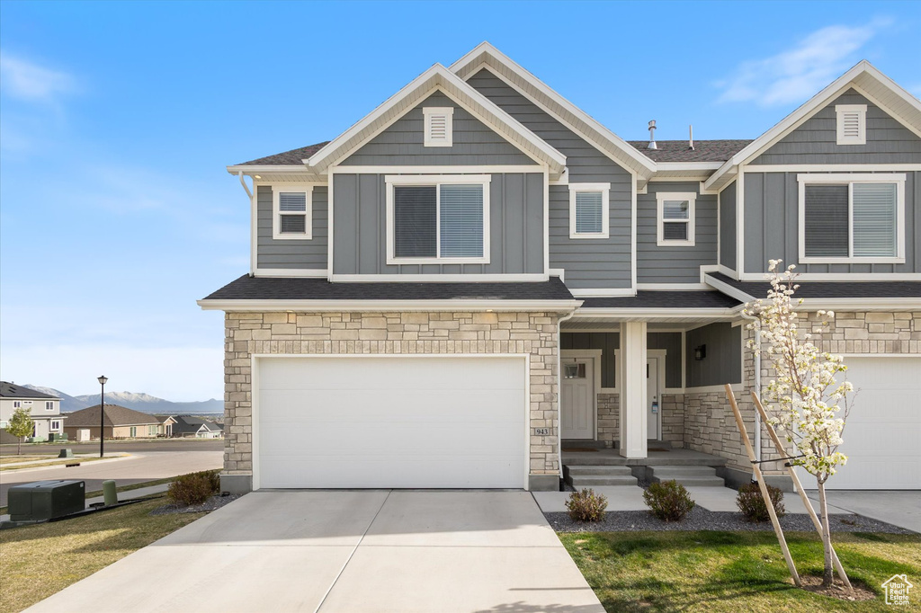 Craftsman house featuring a shingled roof, an attached garage, board and batten siding, driveway, and stone siding