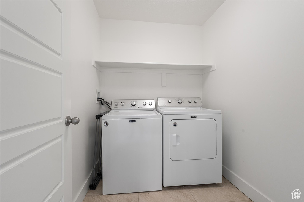 Washroom with washing machine and dryer, baseboards, light tile patterned flooring, and laundry area