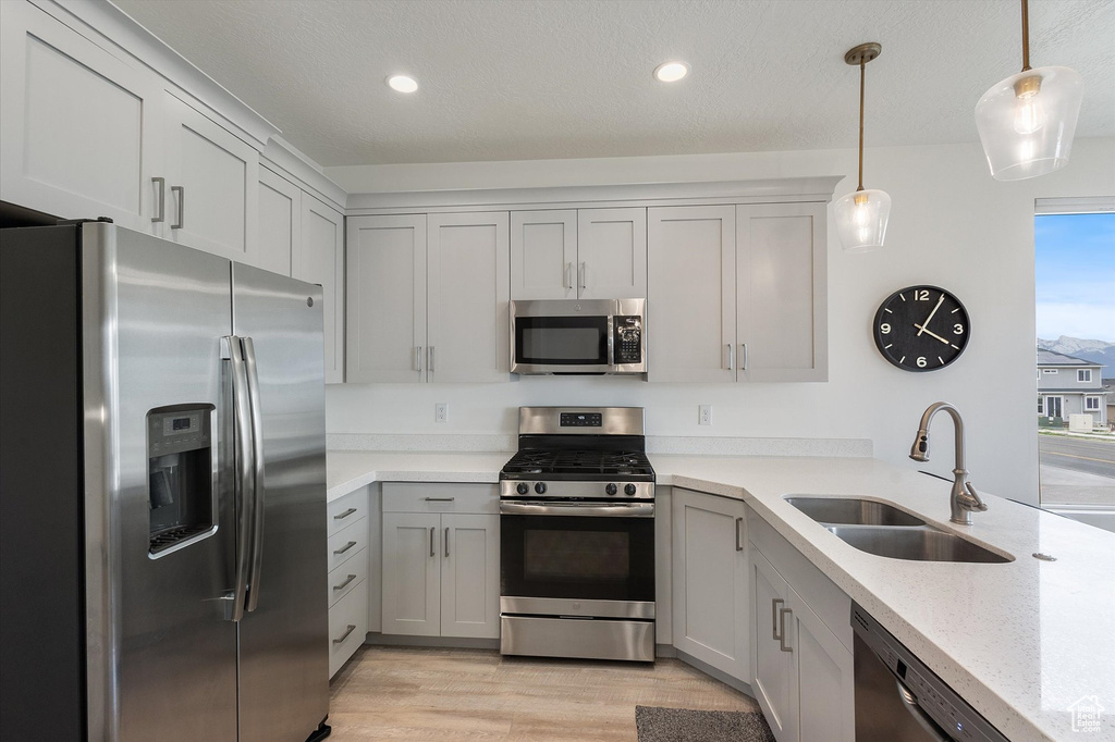 Kitchen with light stone counters, a sink, light wood-type flooring, stainless steel appliances, and decorative light fixtures