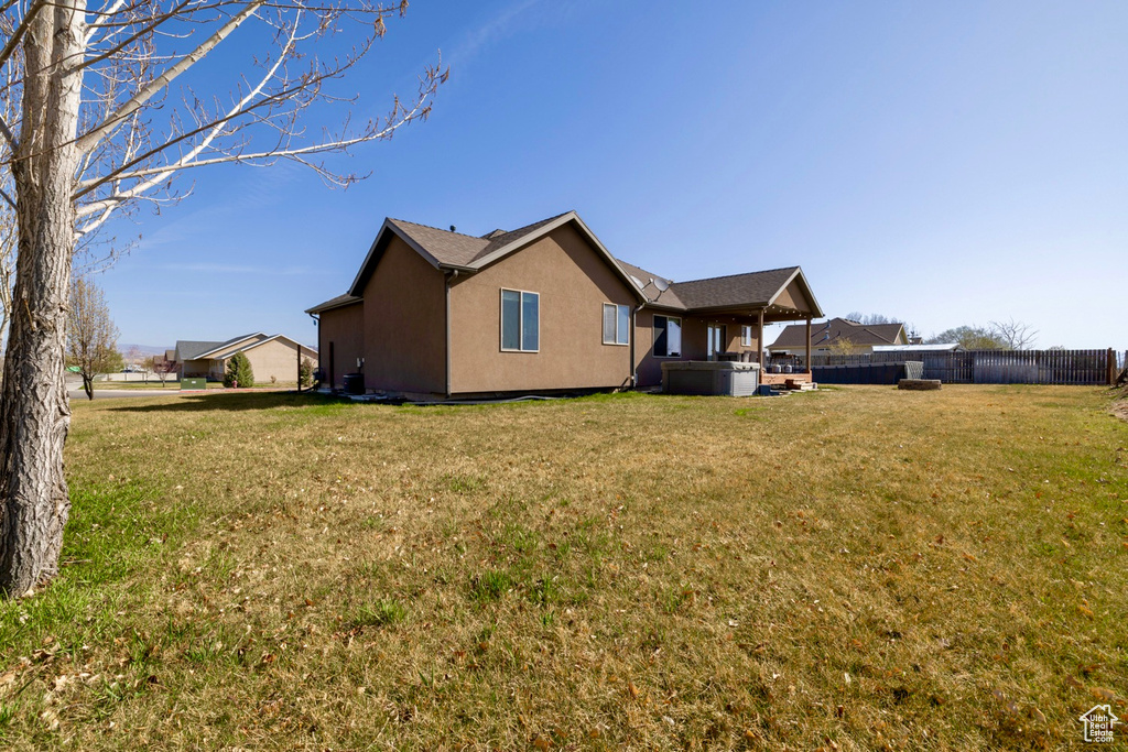 Back of house with a yard, stucco siding, fence, and a hot tub