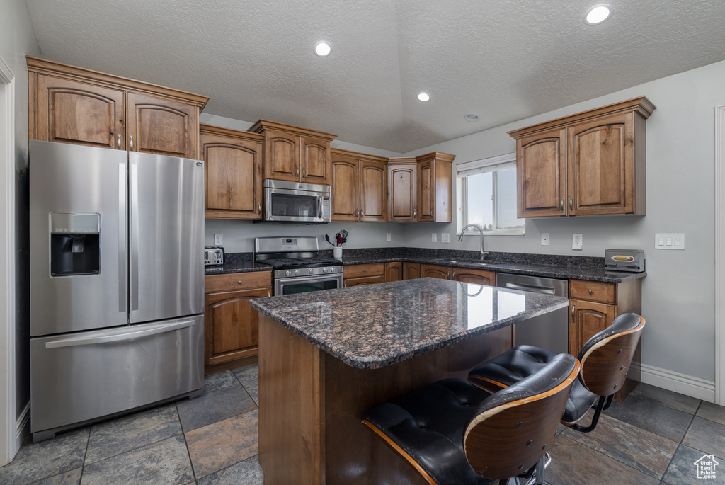 Kitchen with a kitchen bar, stone tile floors, appliances with stainless steel finishes, a sink, and baseboards