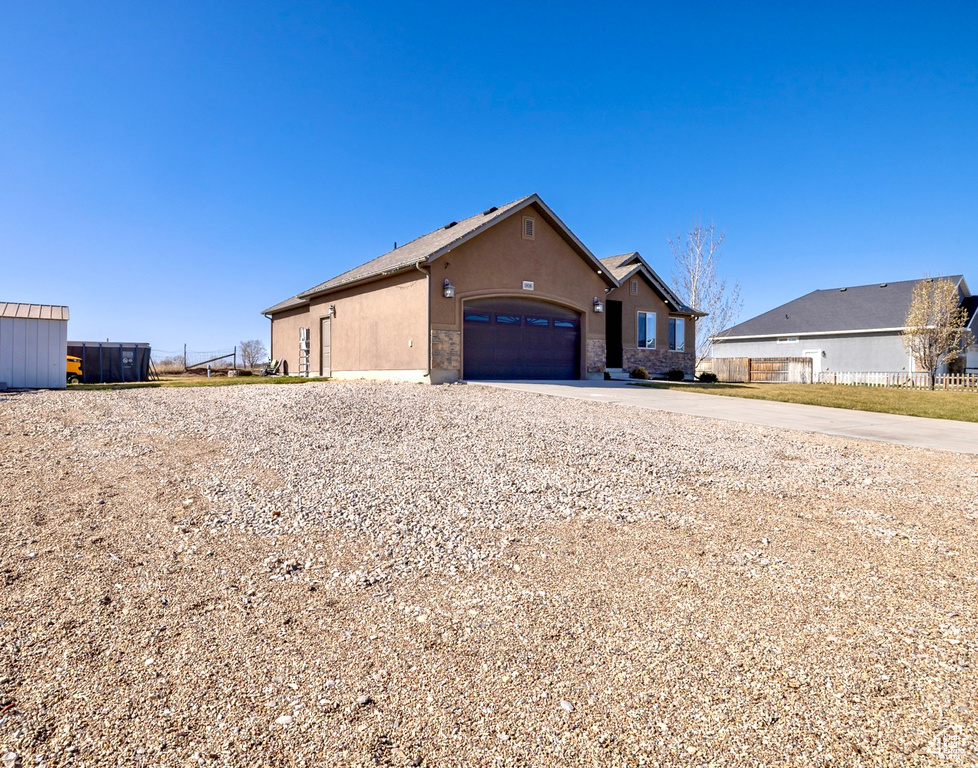View of front of property with stone siding, a garage, concrete driveway, fence, and stucco siding