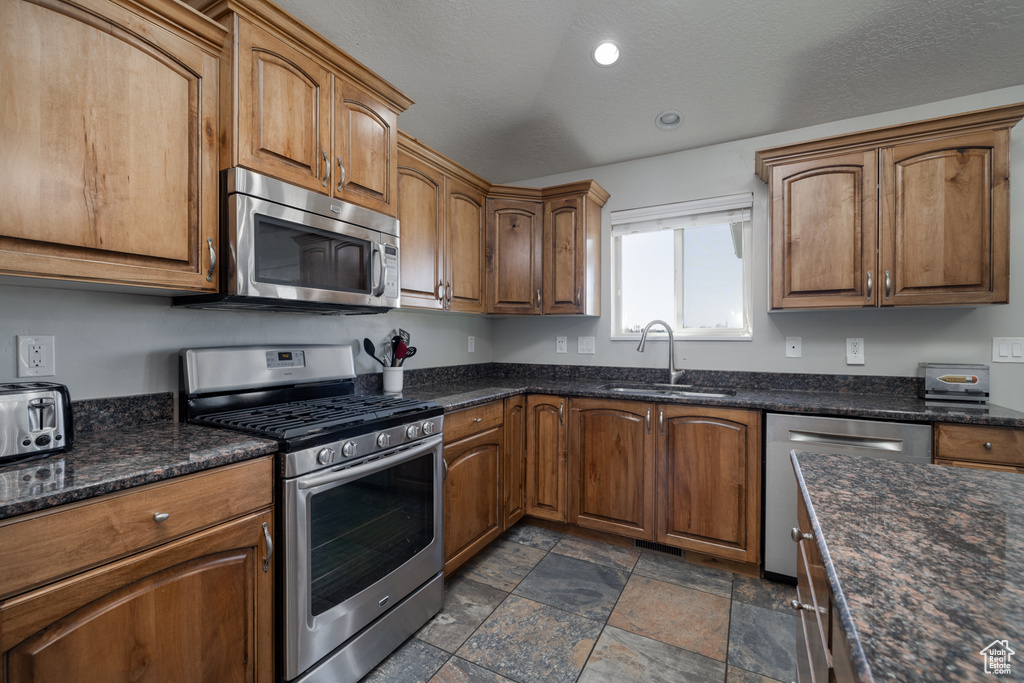 Kitchen featuring brown cabinetry, stone finish floor, recessed lighting, appliances with stainless steel finishes, and a sink