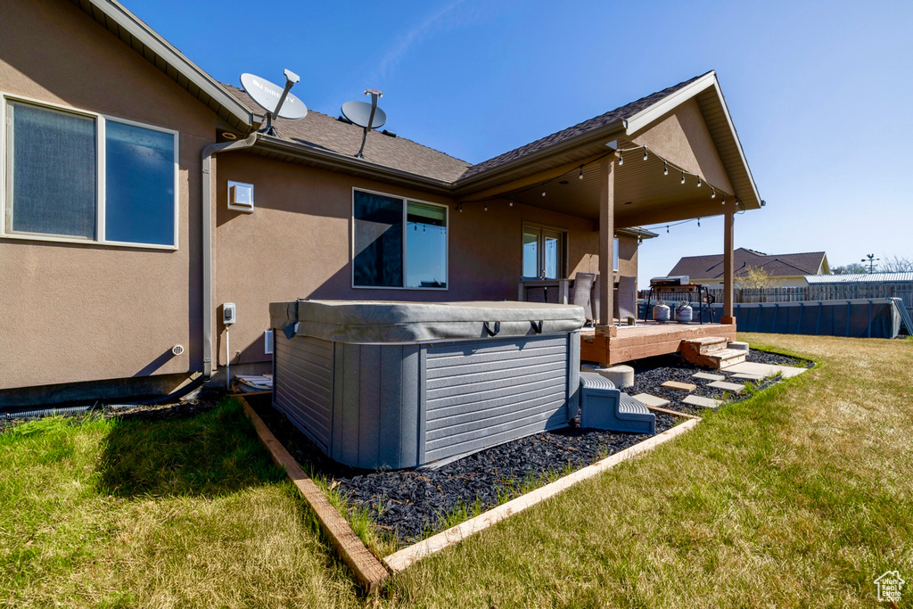 Back of house featuring a yard, fence, stucco siding, and a hot tub