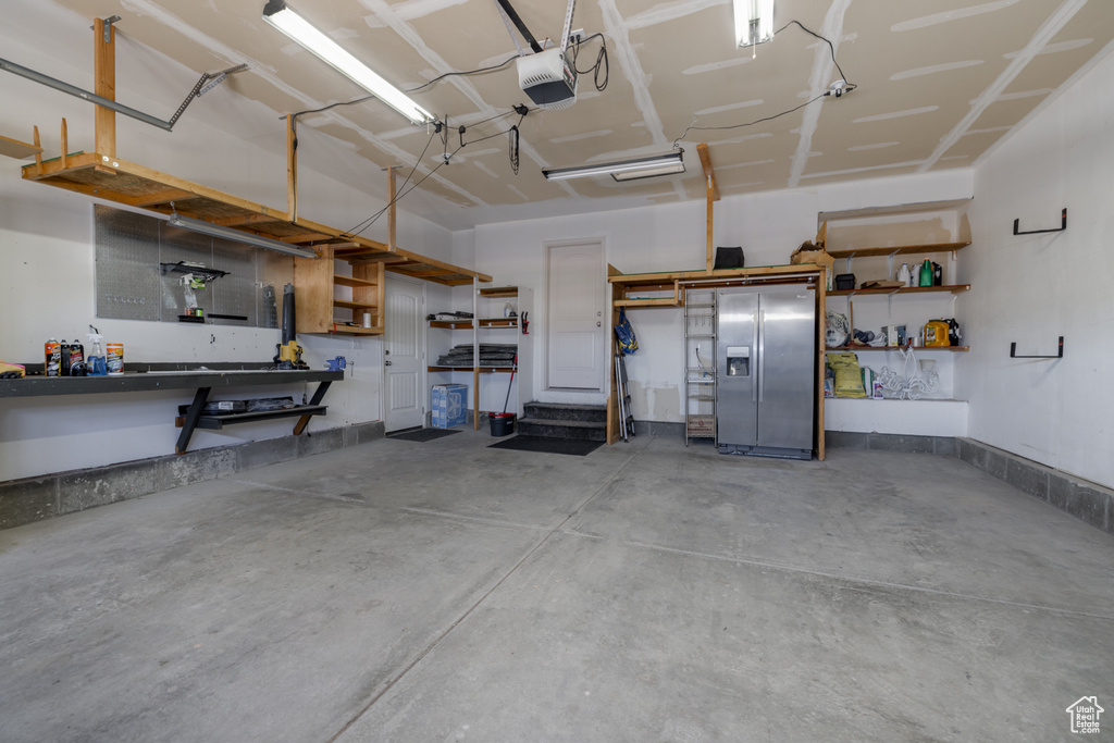 Garage featuring a workshop area, a garage door opener, and stainless steel fridge