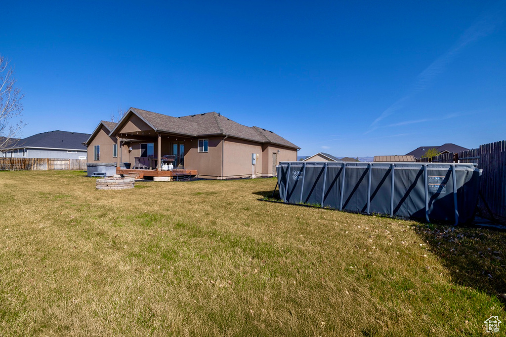 Back of house with a wooden deck, stucco siding, a lawn, fence, and a pool