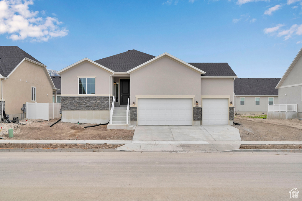 View of front of property featuring stucco siding, stone siding, driveway, and an attached garage