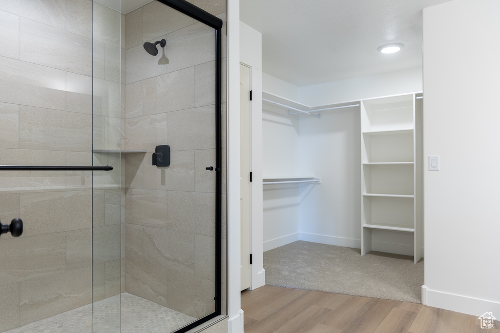 Full bathroom with a walk in closet, wood finished floors, and a stall shower