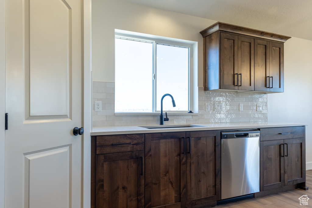 Kitchen featuring light countertops, dishwasher, a sink, light wood-style floors, and tasteful backsplash