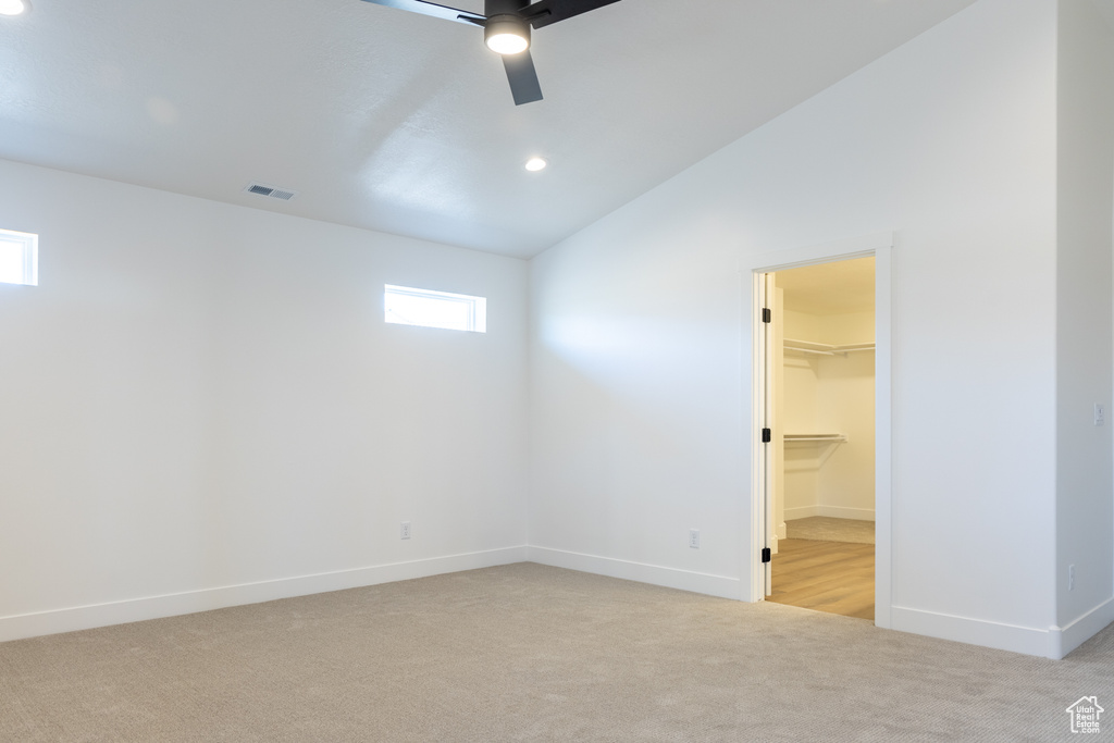 Unfurnished bedroom featuring vaulted ceiling, a walk in closet, light colored carpet, baseboards, and visible vents