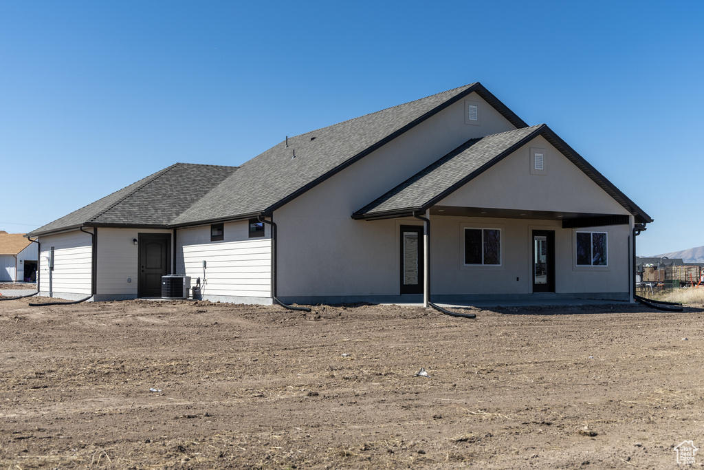 Back of house with a shingled roof and central AC