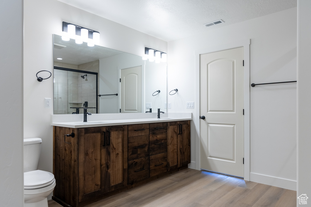 Bathroom with wood finished floors, a stall shower, double vanity, toilet, and visible vents