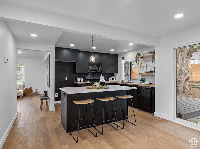 Kitchen with a center island, light wood-style flooring, dark cabinets, light countertops, and black appliances