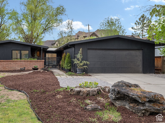 Mid-century modern home featuring an attached garage, concrete driveway, and fence