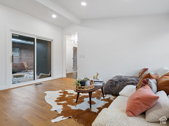 Living room featuring recessed lighting, wood finished floors, visible vents, baseboards, and lofted ceiling with beams