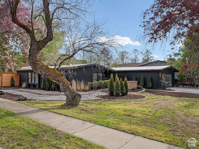 Mid-century inspired home featuring concrete driveway, a front lawn, fence, and a garage