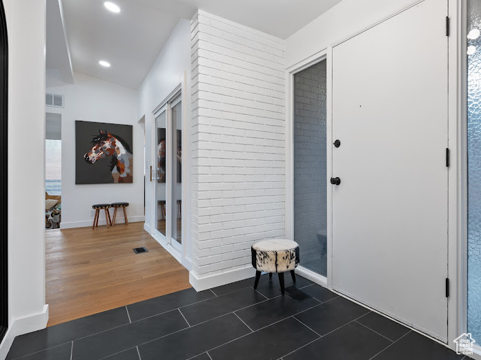 Interior space featuring dark tile patterned flooring, visible vents, recessed lighting, and vaulted ceiling