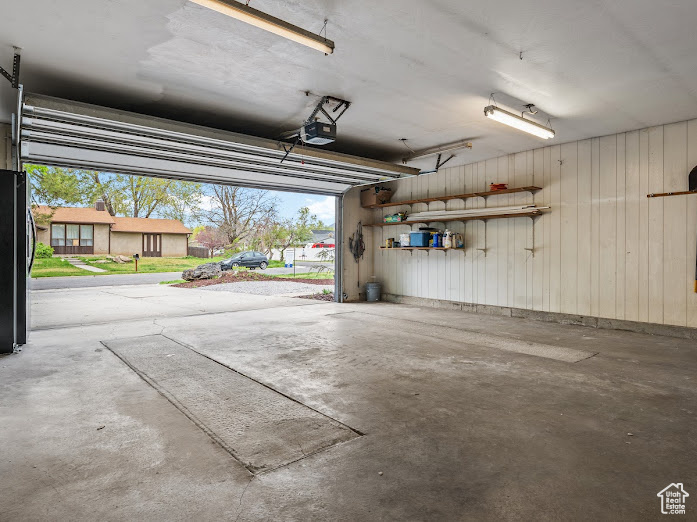 Garage with wood walls, freestanding refrigerator, and a garage door opener
