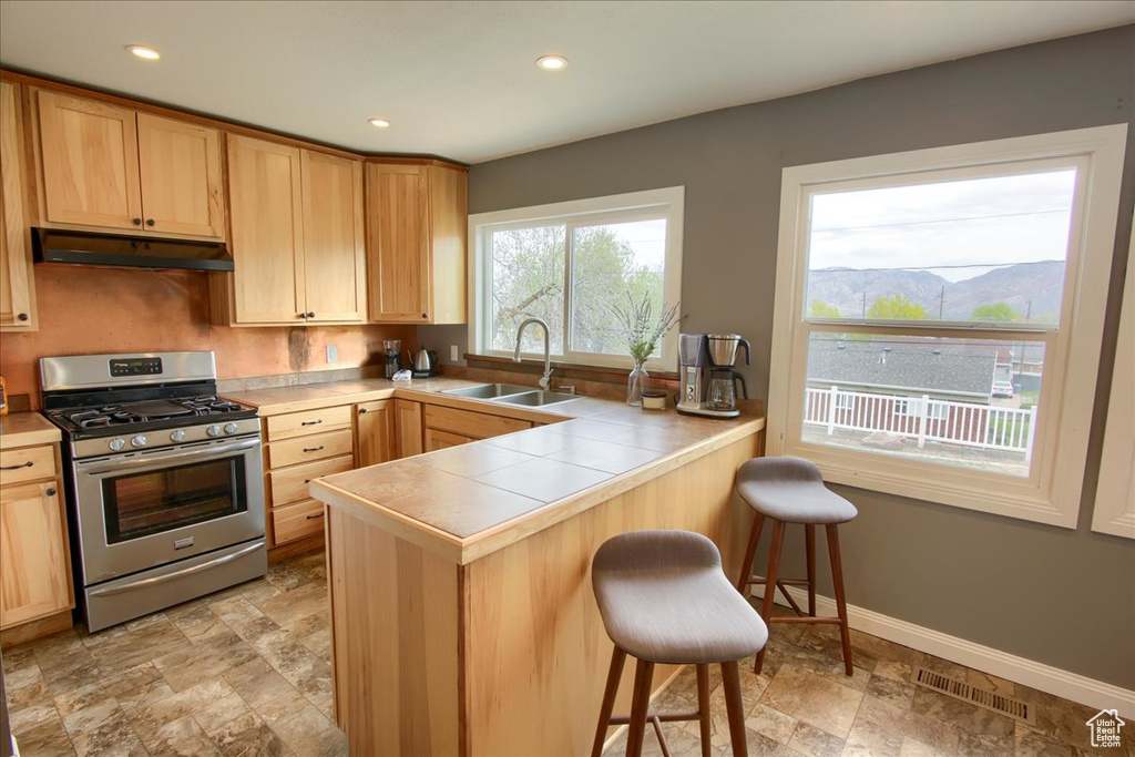 Kitchen featuring under cabinet range hood, a breakfast bar, visible vents, stainless steel range with gas stovetop, and a sink