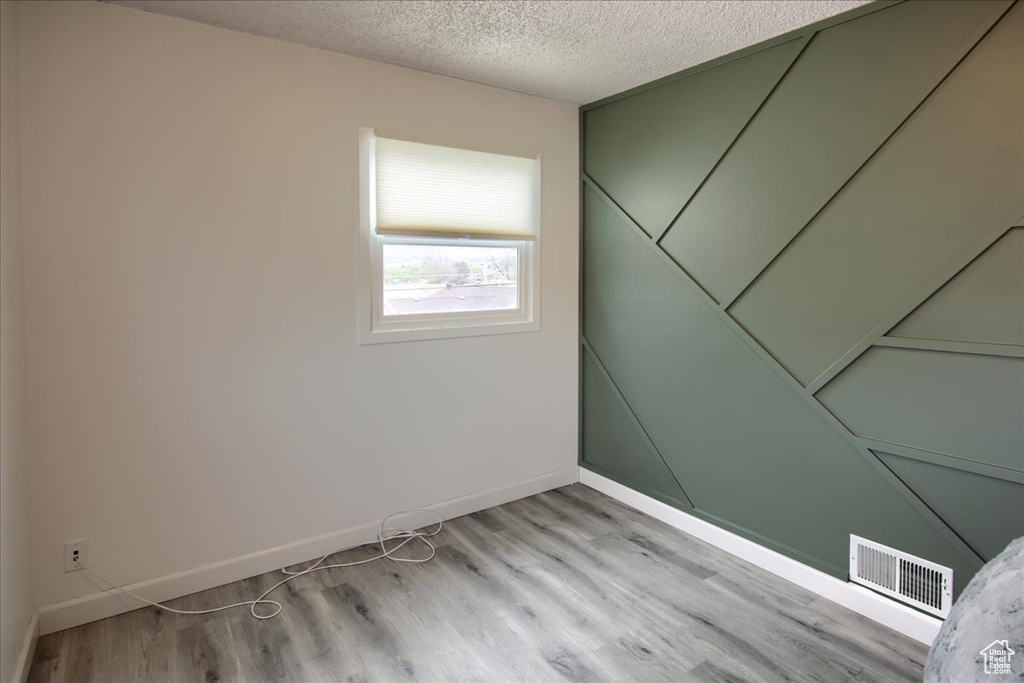 Unfurnished room with baseboards, light wood-style flooring, visible vents, and a textured ceiling