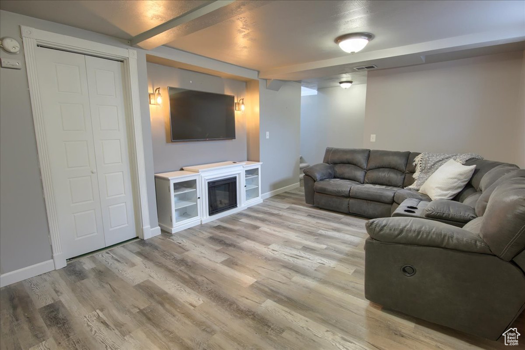 Living area with baseboards, beamed ceiling, light wood-style floors, and visible vents