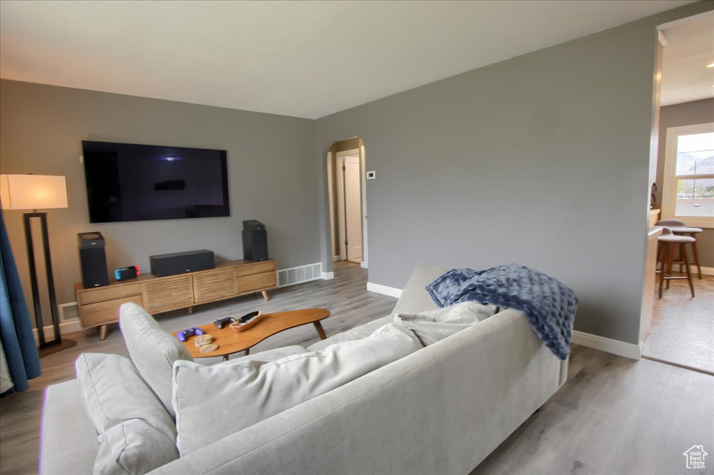 Living area featuring arched walkways, light wood-type flooring, visible vents, and baseboards
