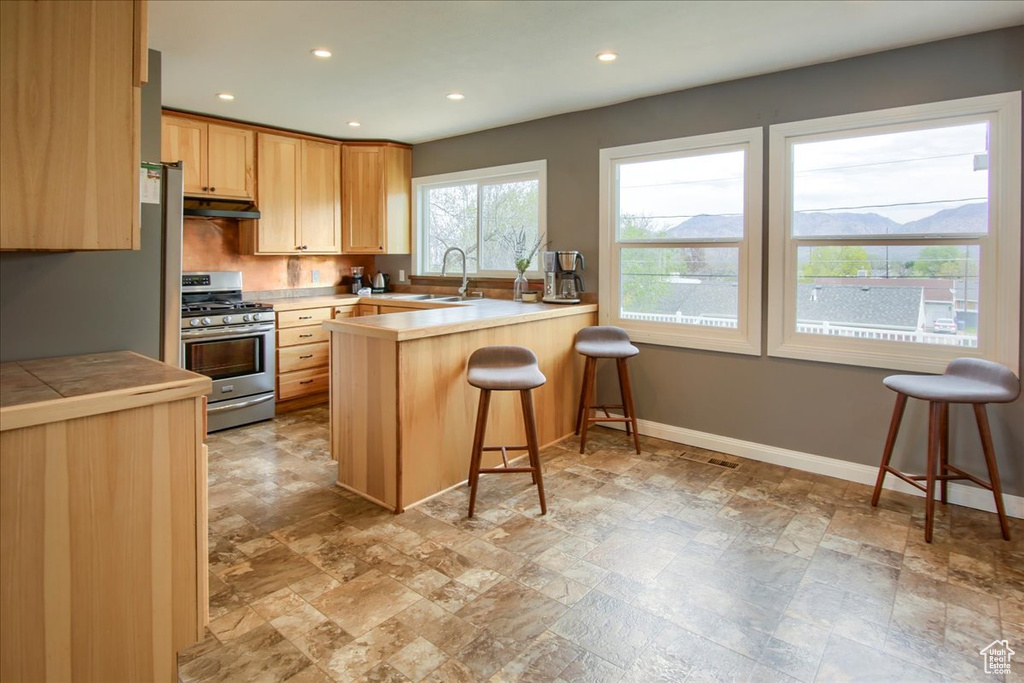 Kitchen with a sink, a kitchen bar, a peninsula, under cabinet range hood, and gas stove