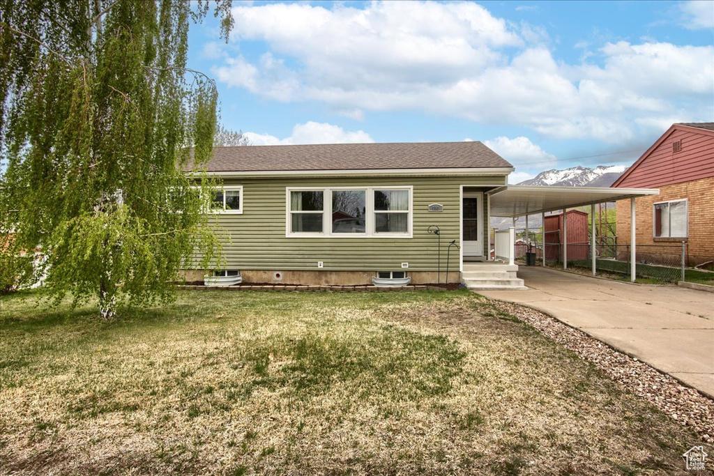 View of front facade with roof with shingles, a carport, concrete driveway, fence, and a front yard
