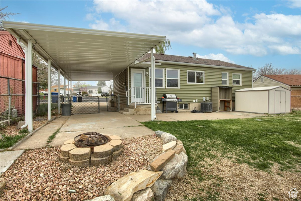 Rear view of property with a lawn, an outdoor fire pit, fence, an outbuilding, and a storage unit