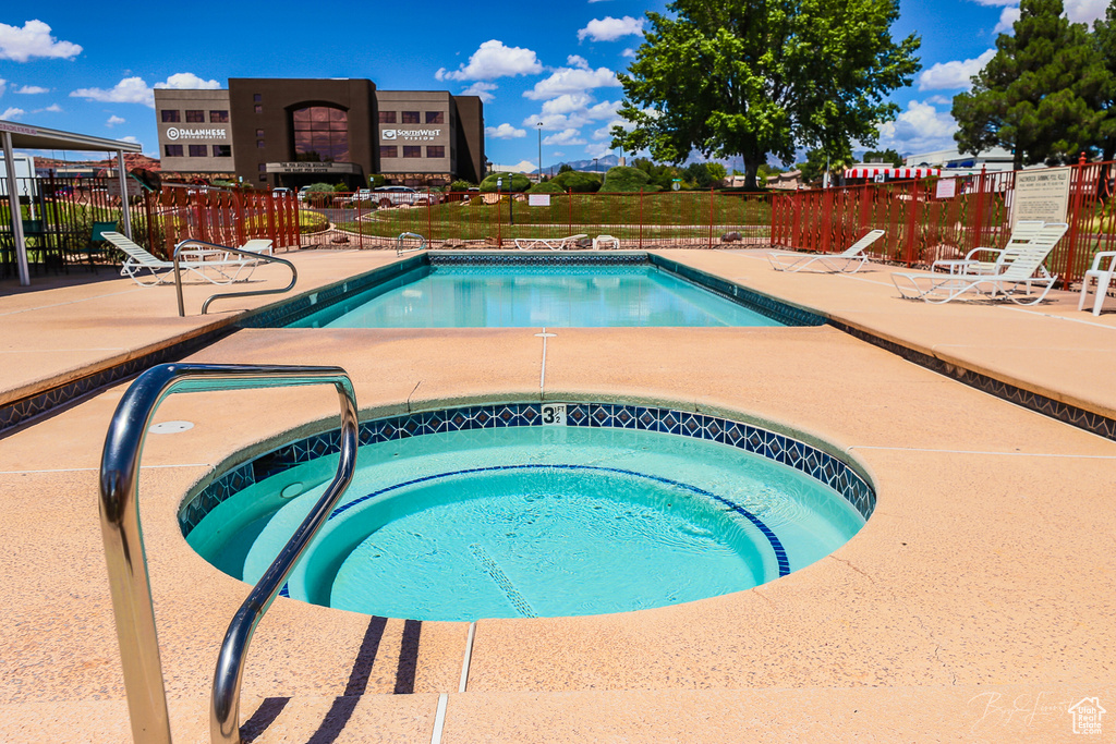 Community pool with fence, a hot tub, and a patio